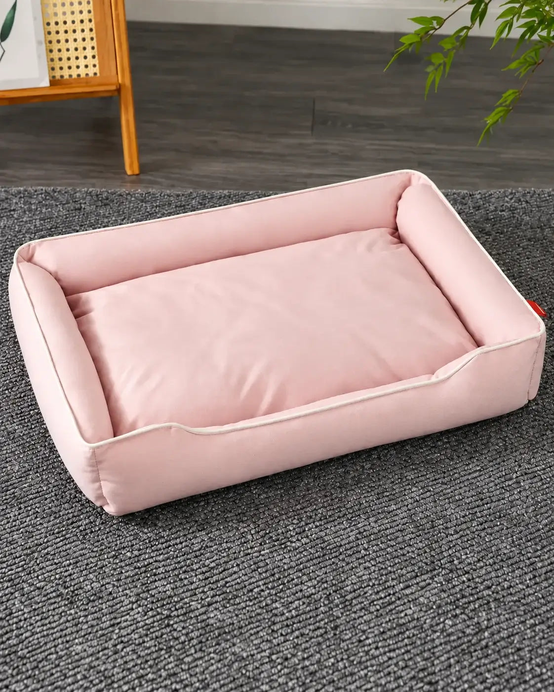 Pale pink waterproof dog sofa bed with cream piping on a gray rug